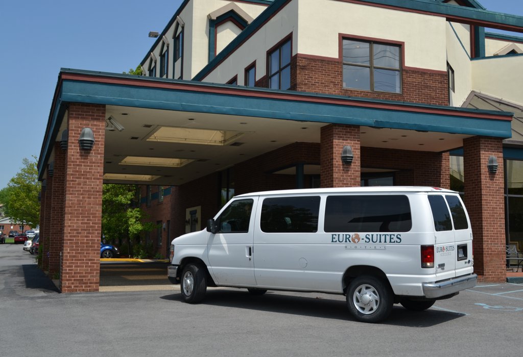 A white van is parked in front of a hotel exterior with a brick facade and awning.
